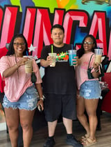 Three people holding beverages standing in front of a colorful graffiti wall backdrop