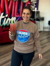 Woman smiling and holding a red beverage while wearing a Duncanville Nutrition sweatshirt