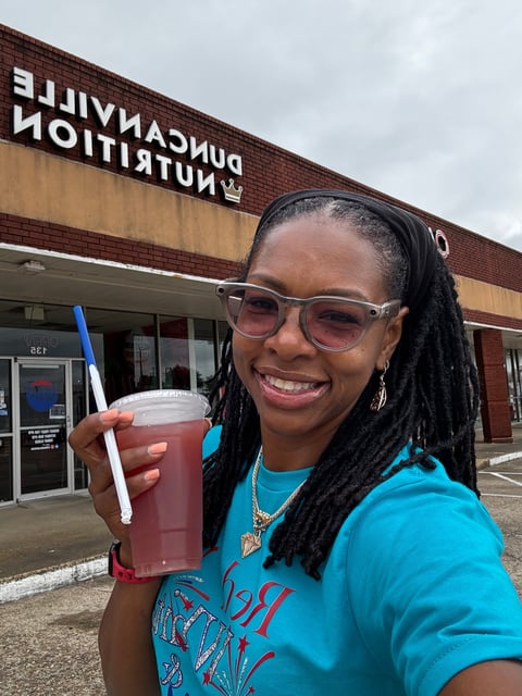 Smiling woman wearing glasses and blue shirt holding a red beverage cup outside Duncanville Nutrition